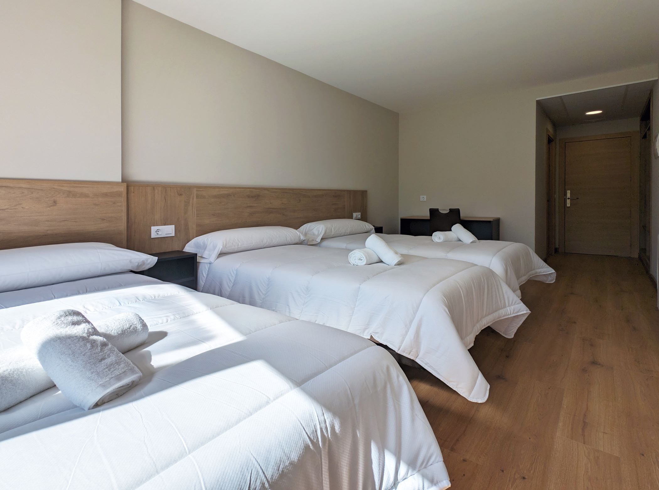 A hotel room with three beds, wooden headboards, and a wooden floor.