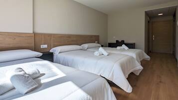 A hotel room with three beds, wooden headboards, and a wooden floor.
