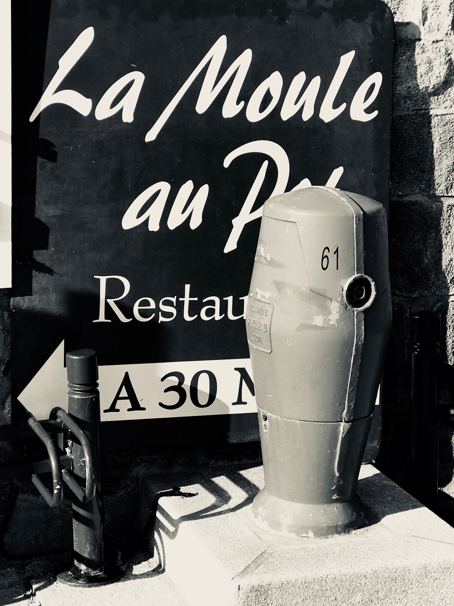 En svart skylt med vit text som visar ”La Moulade au Petit” och ”Restaurang”, samt en pil som pekar åt vänster.
