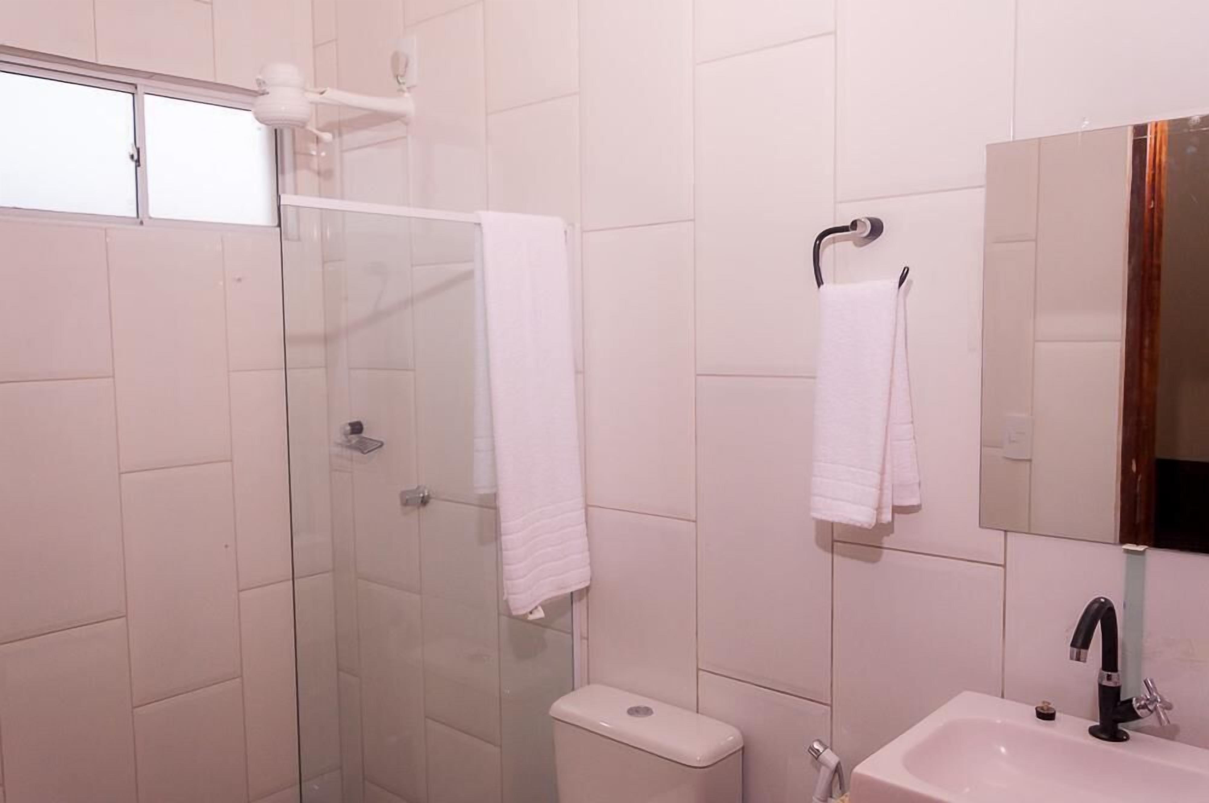 A bathroom with a glass shower enclosure, a white toilet, a sink with a black faucet, and a mirror with a wooden frame.