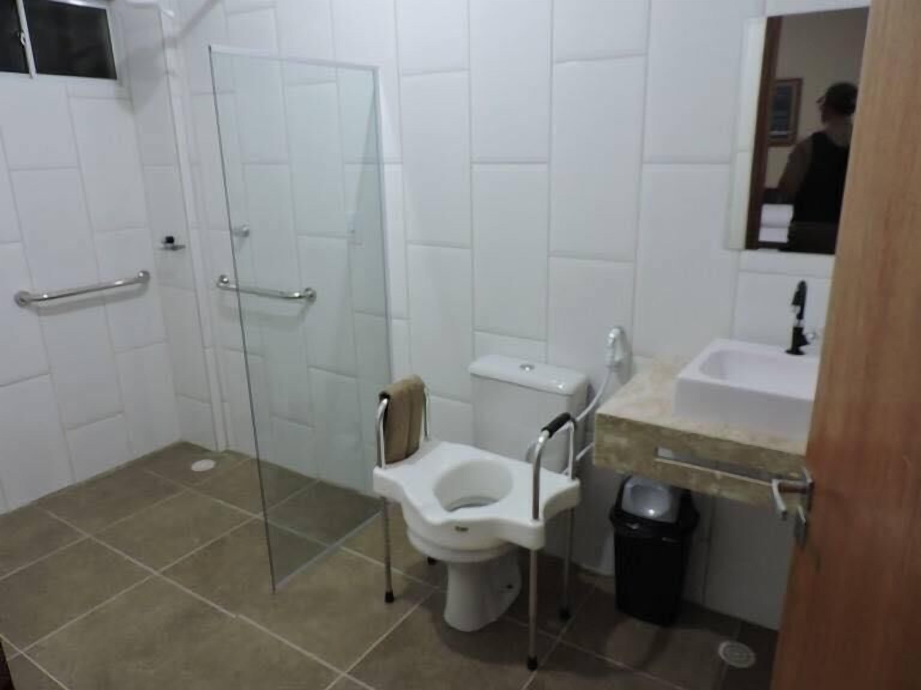 Un baño con cabina de ducha de vidrio, inodoro, lavabo y cubo de basura.