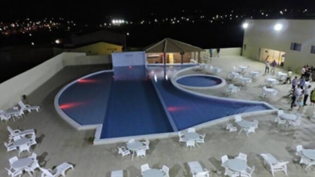 Un espace piscine extérieur avec des chaises longues et des tables blanches, entouré d’un petit muret.