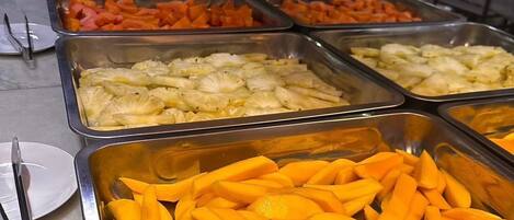 Un bufé con diversos alimentos, incluyendo piña, mango y zanahorias.