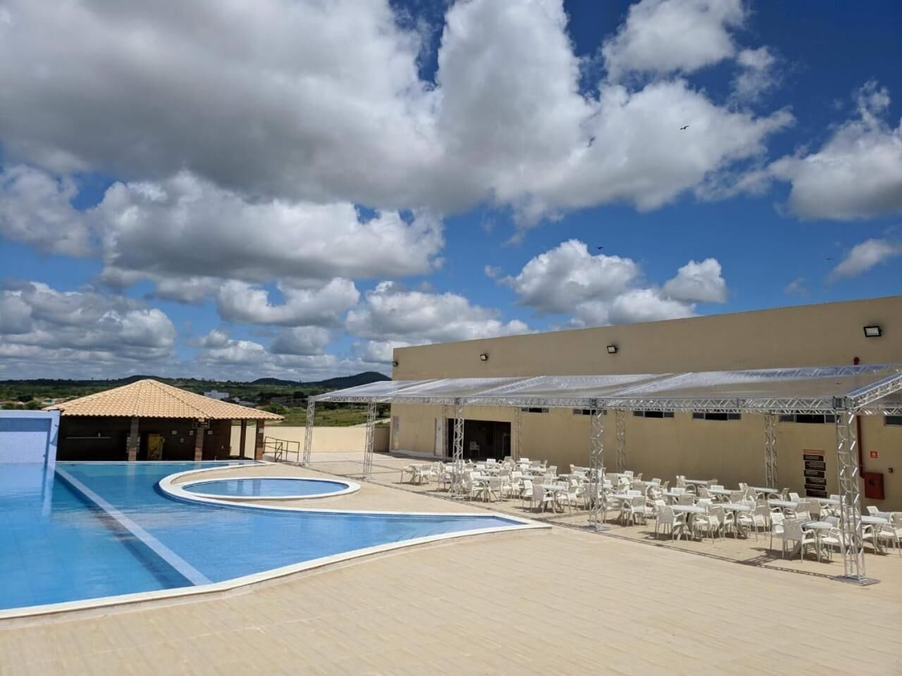 A swimming pool area with multiple pools, covered seating areas, and a building with a flat roof.