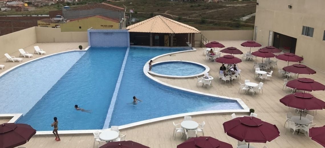 A swimming pool with a children's section, surrounded by outdoor seating and umbrellas.