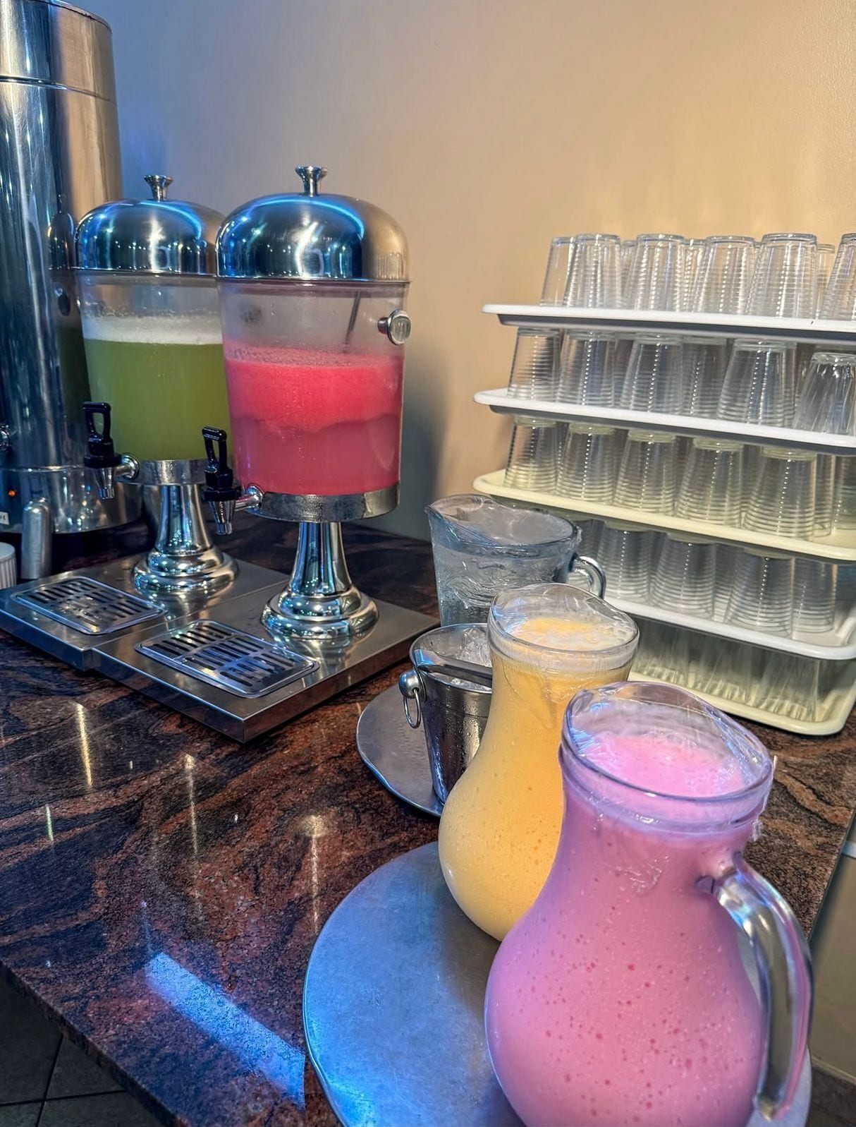 Un espace dédié aux boissons, équipé de plusieurs distributeurs et d’un plateau rempli de gobelets en plastique.