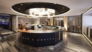 A modern reception area with a circular counter labeled "ESH & FRUITY," featuring a marble countertop, a digital screen, and a seating area with two chairs. - ALFIT HOTEL & BAR AKASAKA (Tokyo)