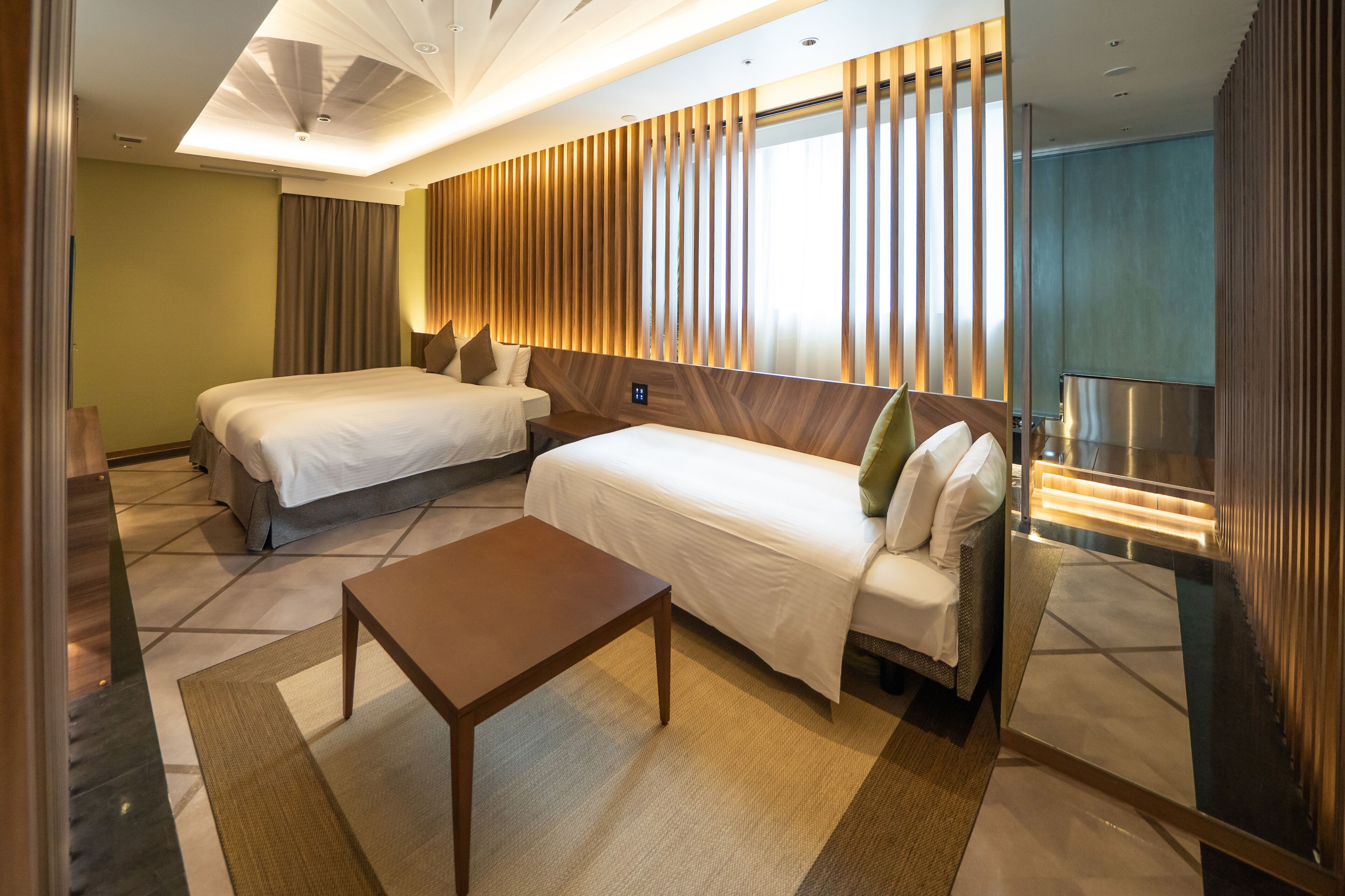 A hotel room with two beds, a small table, and a large mirror.