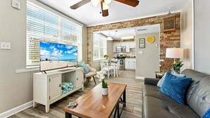 A living room with a TV, sofa, coffee table, and a view of the kitchen and dining area. - 🌴Steps to Sand @ Clearwater Beach Suites | Heated Pool • Split Floor Plan ➠ CBS 206 (Clearwater Beach)