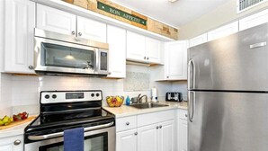 Una cocina con armarios blancos, un refrigerador de acero inoxidable, un microondas y un horno.