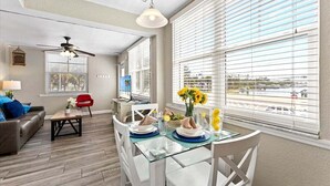 A modern living room with a dining area, large windows with blinds, a ceiling fan, and a view of the outside. - 🌴Steps to Sand @ Clearwater Beach Suites | Heated Pool • Split Floor Plan ➠ CBS 206 (Clearwater Beach)