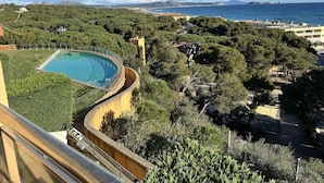 A pool surrounded by lush greenery, overlooking a coastal area with buildings and mountains in the distance.