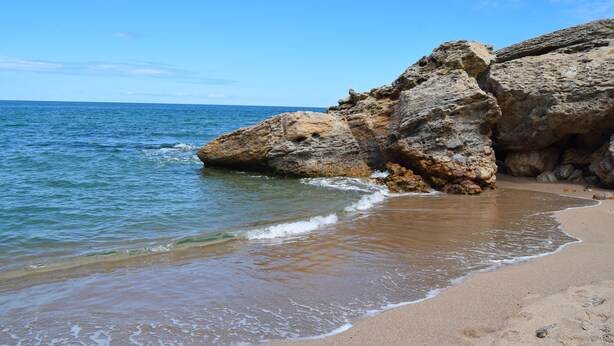 A beach with clear blue water, rocky formations, and a sandy shore.