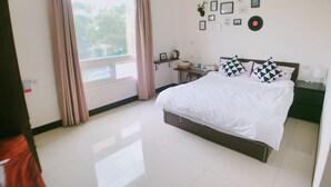 Camera d'albergo con un letto grande, un comodino, una finestra con tende, una parete con quadri e una ventola a soffitto.