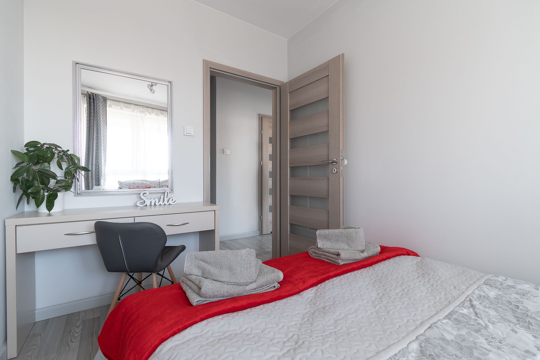 A bedroom with a bed, a desk, a chair, a mirror, and a wardrobe.