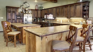 Una cocina amplia con armarios de madera, una isla central con taburetes de bar y una pata de gallo para colgar ollas.