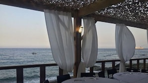 Un área de comedor al aire libre con mesas dispuestas para dos, con vista al mar.