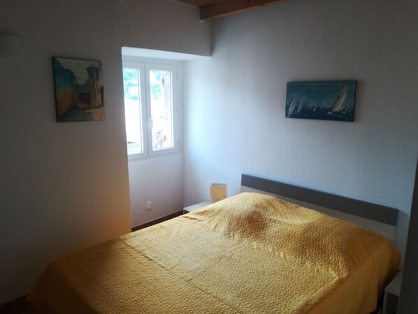 Un dormitorio con una cama, una ventana y dos cuadros en las paredes.