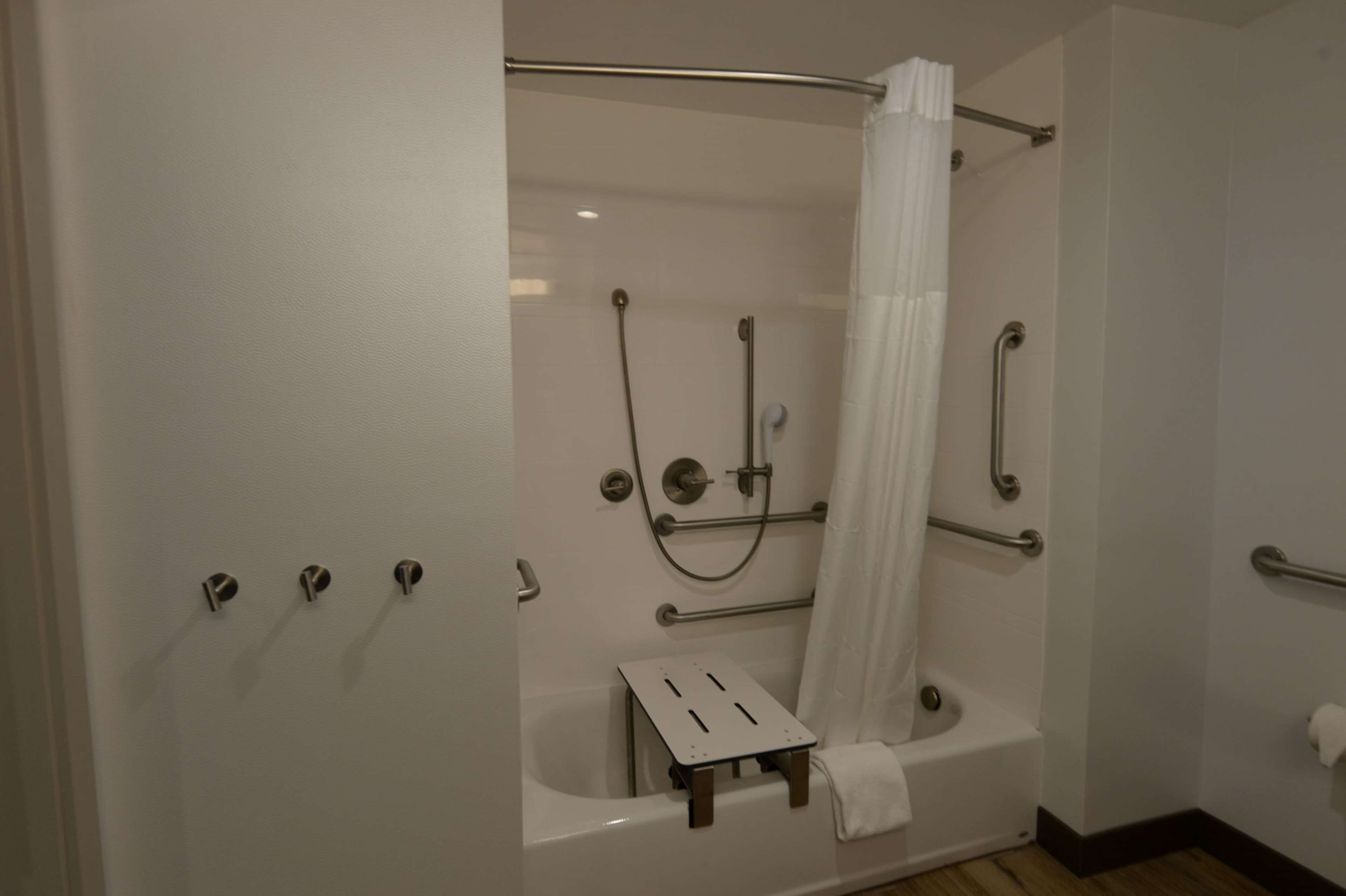A walk-in shower with a bathtub, grab bars, and a small step stool.