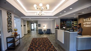 Uma área de recepção de hotel com design moderno, incluindo um balcão de atendimento, zona de estar e uma parede decorativa.