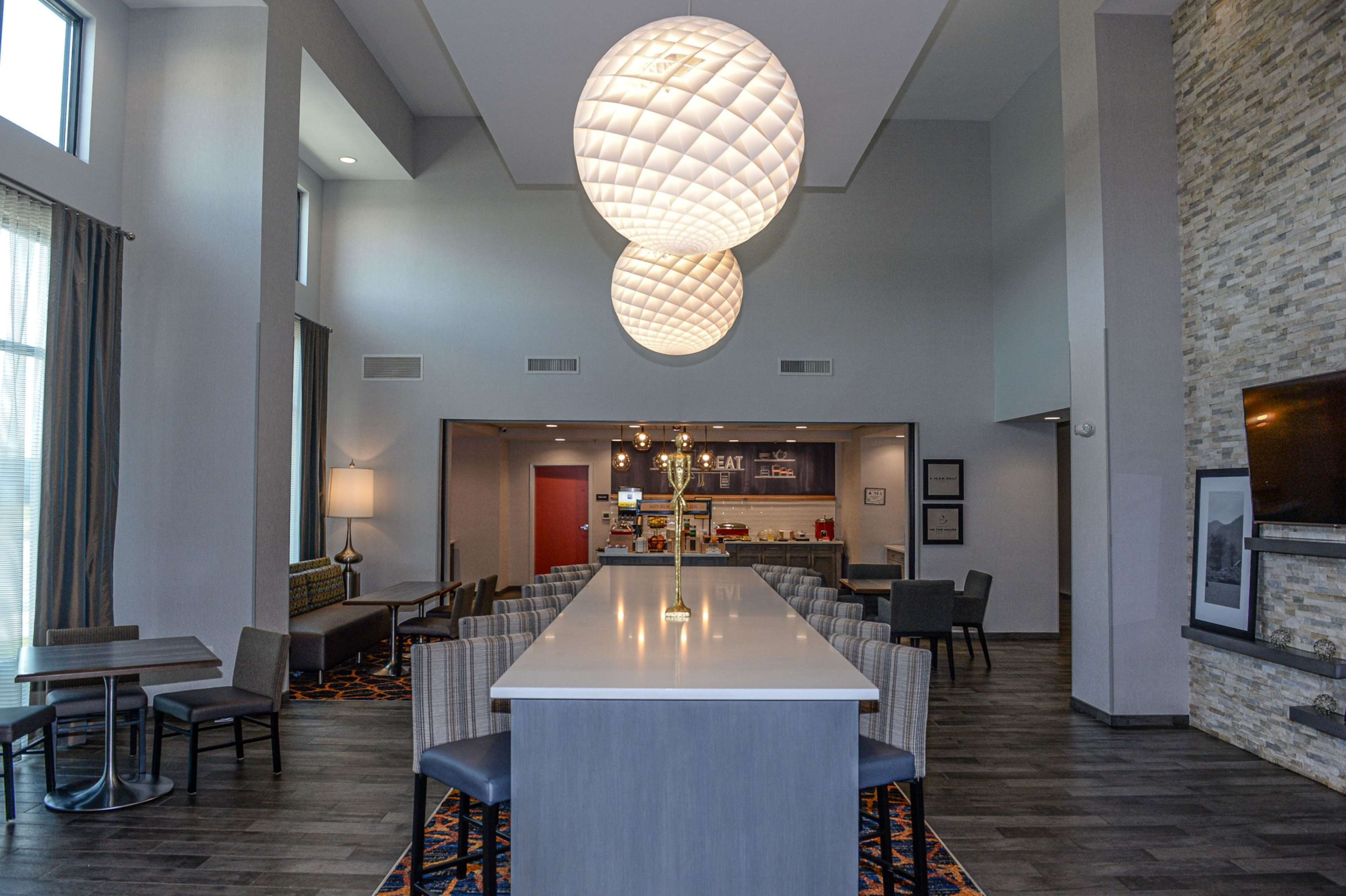 Un hall d’hôtel spacieux, doté d’un long comptoir d’accueil, de plusieurs espaces salon et d’un grand lustre.