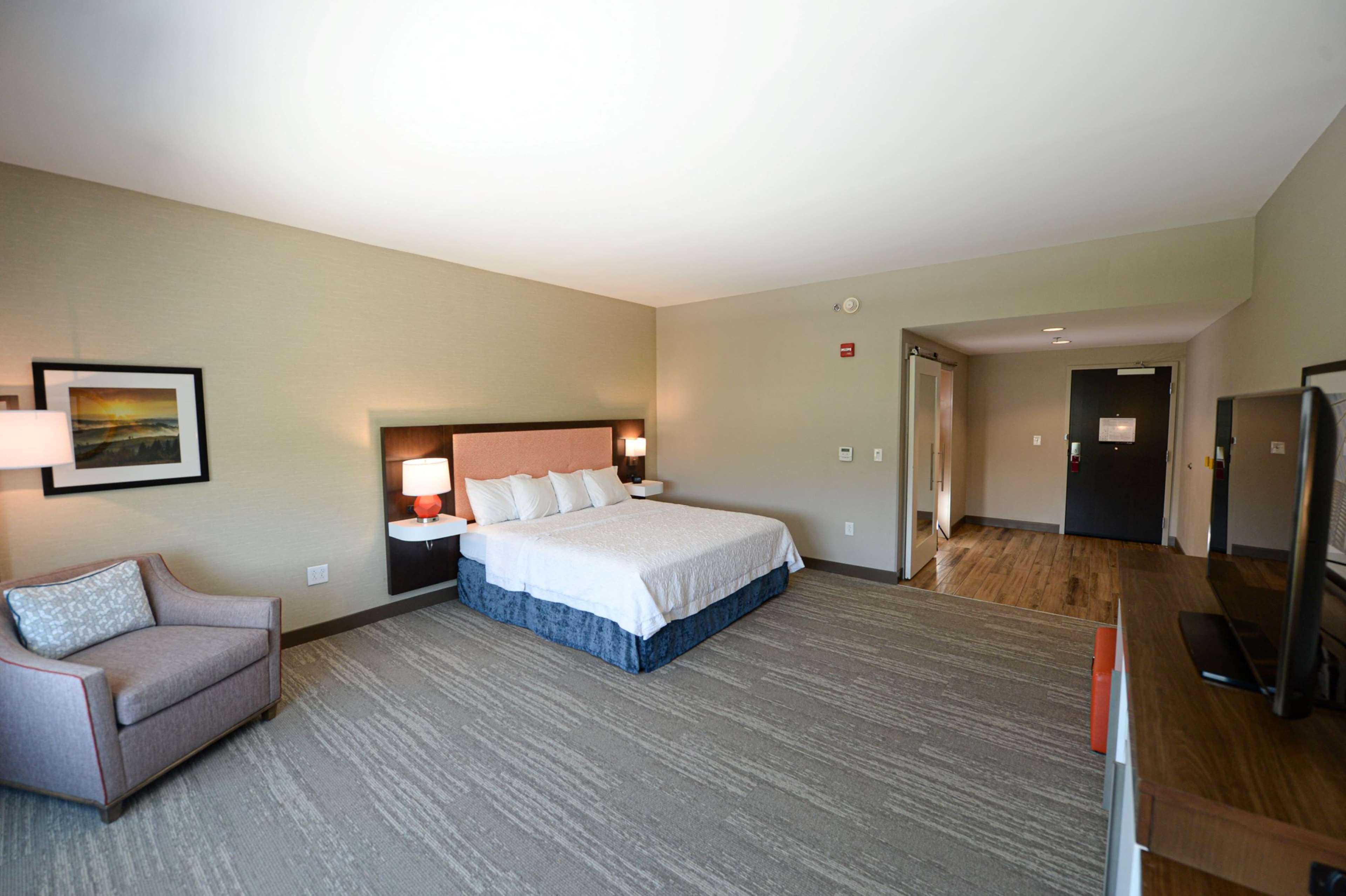 A hotel room with a bed, a chair, a desk, and a television.