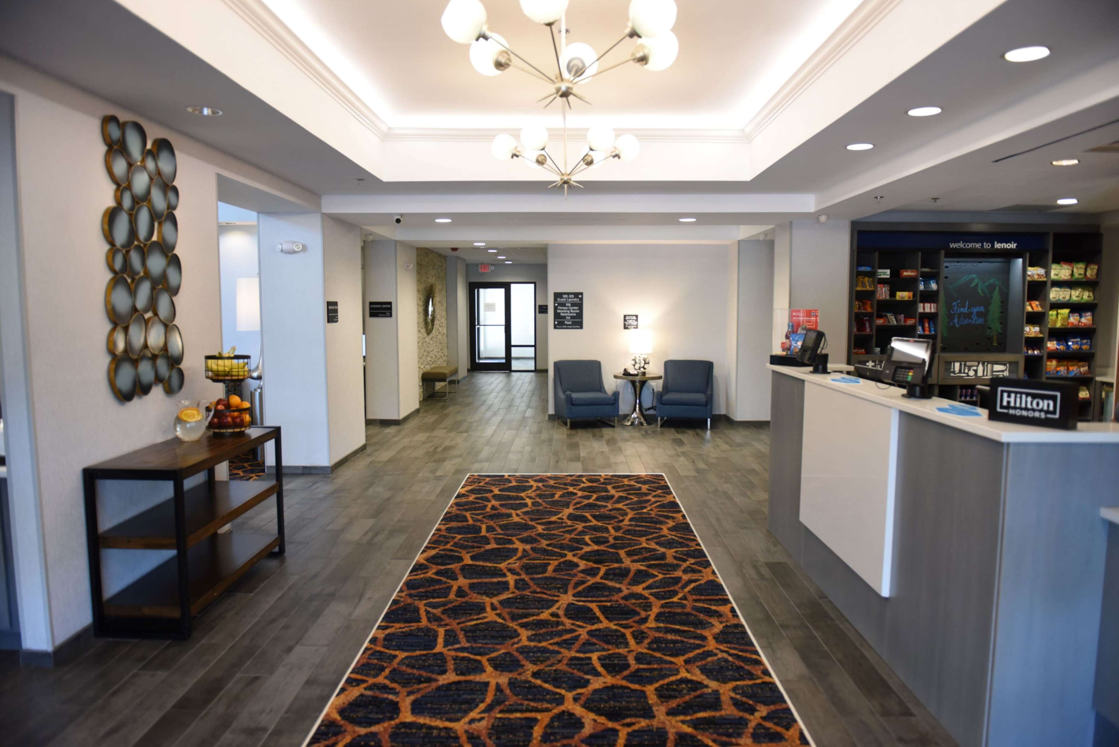 Een hotel lobby met een receptiebalie, een zithoek en een kamerbreed tapijt met dessin.