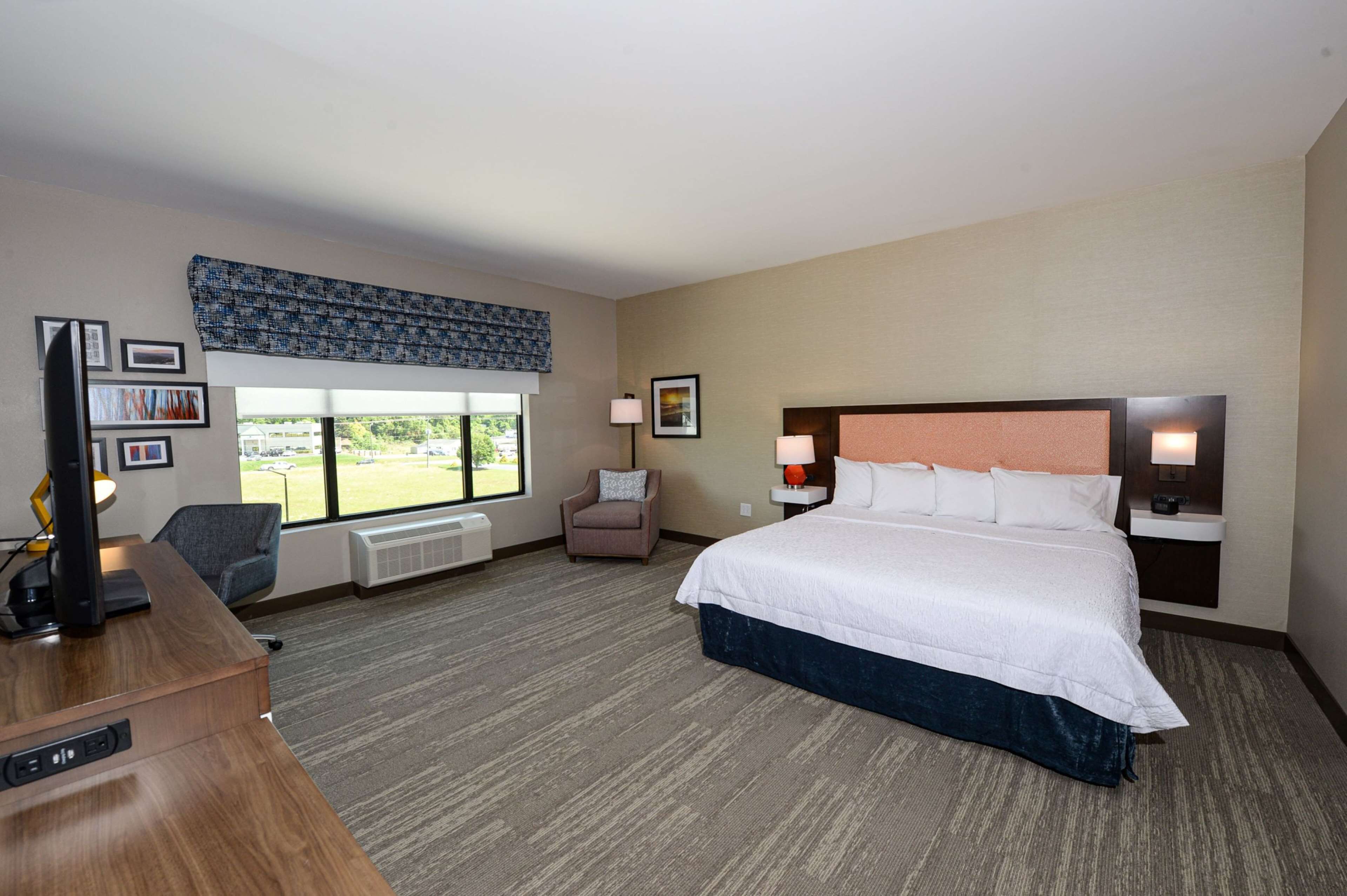 A hotel room with a large bed, a desk, a chair, a window with a view, and a wall-mounted TV.