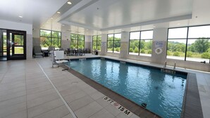 Piscina interior com sinalização clara, chão em azulejo e grandes janelas com vista para o exterior.