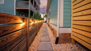 Un étroit sentier bordé de clôtures en bois et de bâtiments, avec un chemin dallé de pierres.