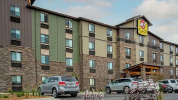 Un hotel de varios pisos con fachada de piedra, numerosas ventanas y un estacionamiento con varios automóviles.