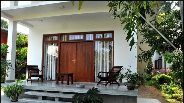A covered porch with a wooden door, two wooden chairs, a small table, and potted plants. - Green Corridor - Ahangama (Ahangama)
