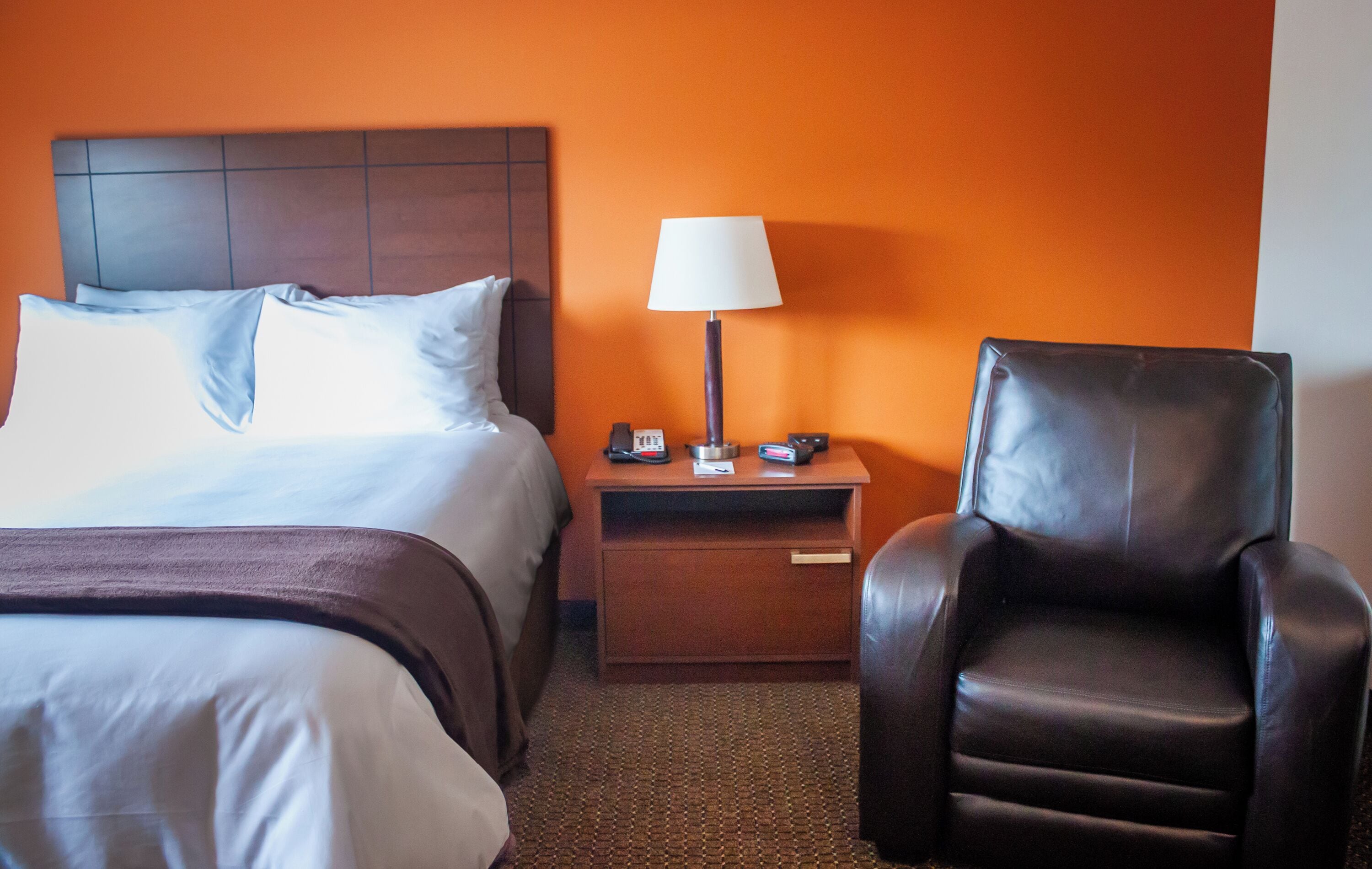 Een hotelkamer met een bed, een nachtkastje met een lamp en een leren fauteuil.