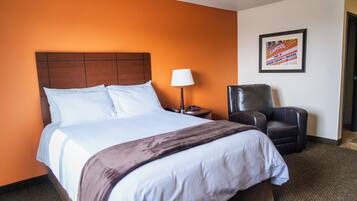 A hotel room with a large bed, a chair, a lamp, and a framed picture on the wall.
