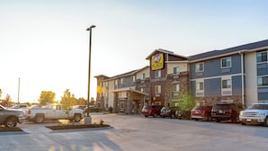 A multi-story hotel with a 'My Place' sign, a parking lot with various vehicles, and a 'Now One' sign. - My Place Hotel - Mount Pleasant (Mount Pleasant)