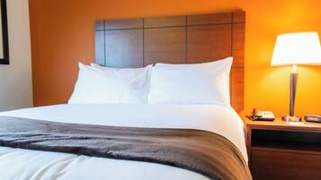 A hotel room with a neatly made bed, a nightstand with a lamp, and a wall-mounted telephone.