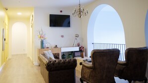 A living room with a sofa, two armchairs, a TV, and a chandelier. - Hi Go Hostel & Suites (Vila Nova de Famalicao)
