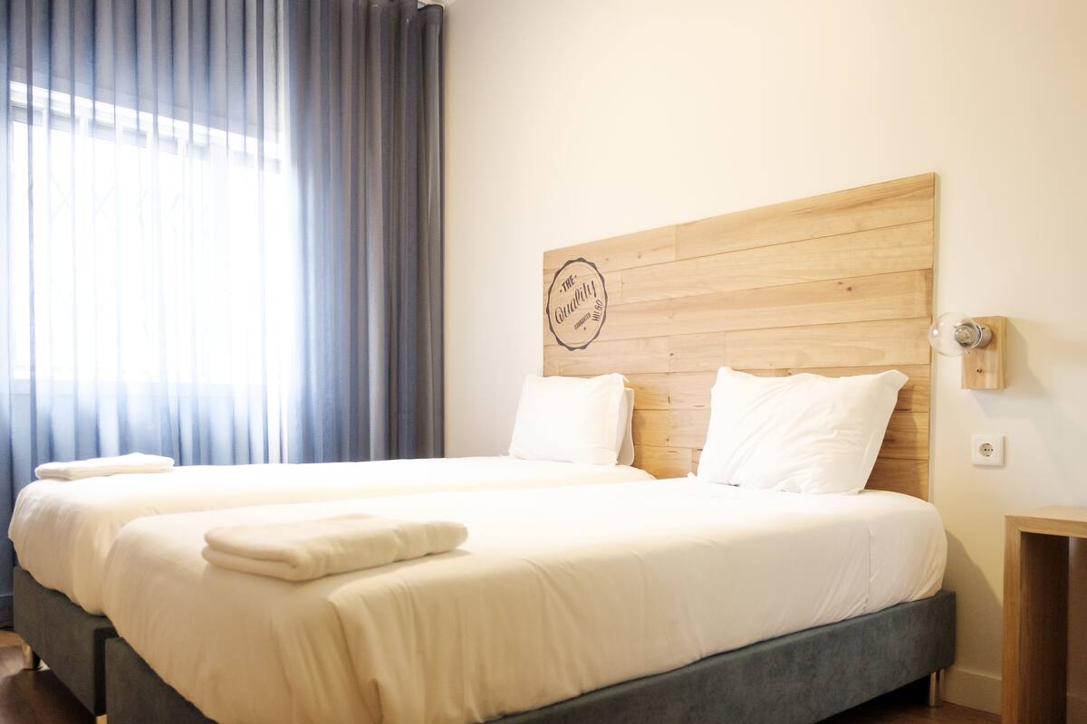 Une chambre d’hôtel avec deux lits, une tête de lit en bois et un luminaire fixé au mur.