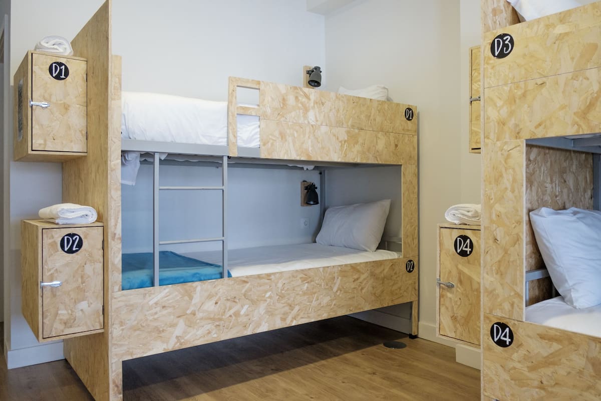 Une chambre avec des lits superposés en bois, une échelle et des armoires de rangement étiquetées D1, D2, D3 et D4.