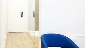 A hallway with a blue chair, a white door, and a glass partition. - Hi Go Hostel & Suites (Vila Nova de Famalicao)