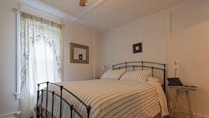 A bedroom with a bed, a bedside table with a lamp, a mirror on the wall, and a window with curtains. - The Woodbine Inn (Palenville)