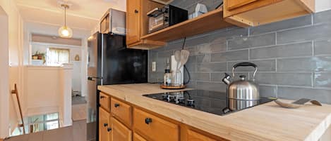 Une cuisine avec des meubles de rangement en bois, un réfrigérateur noir et une bouilloire en acier inoxydable posée sur le plan de travail.