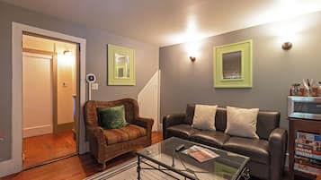 A living room with a wicker chair, a leather sofa, a glass coffee table, and a bookshelf with books.