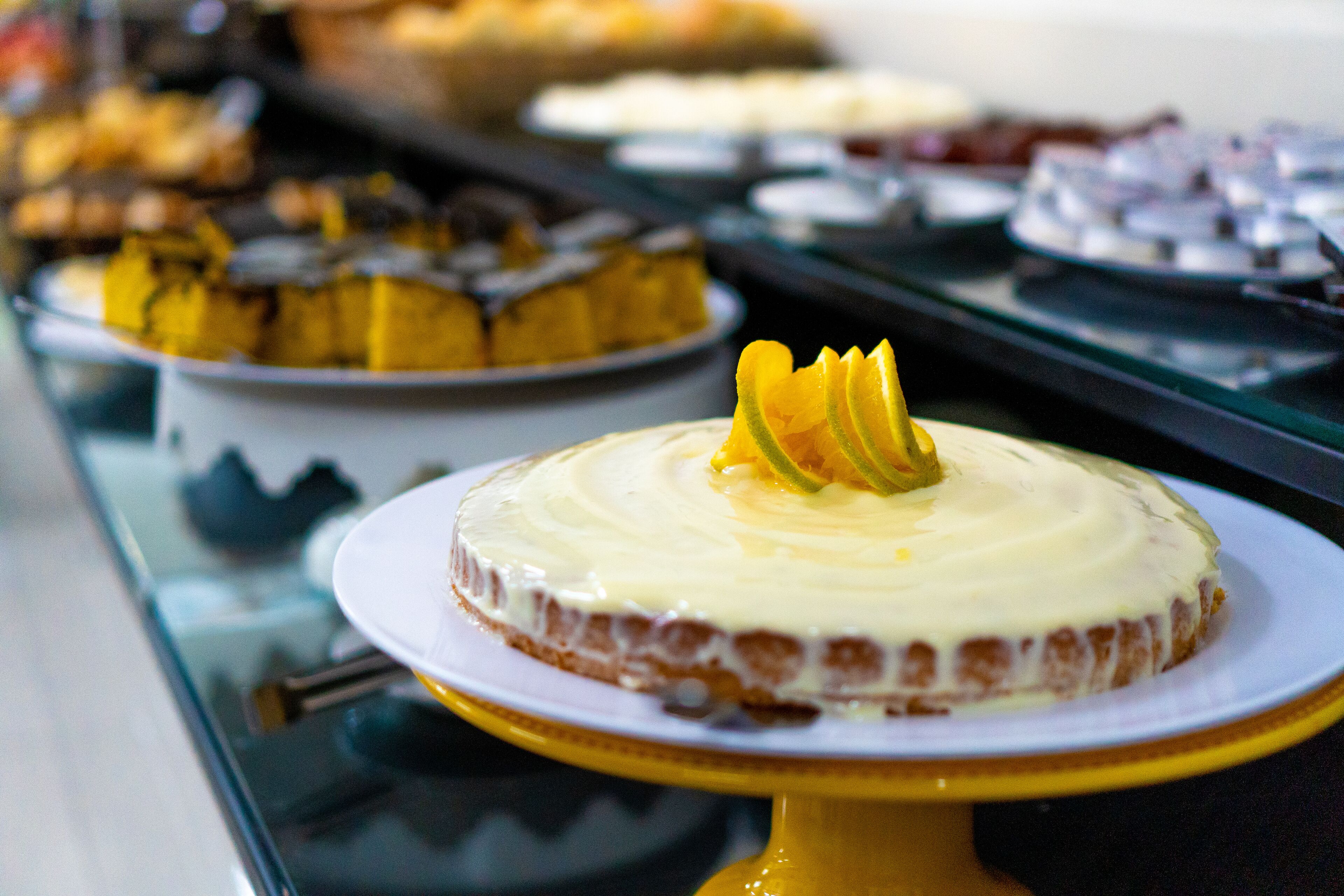 Un bufé con diversos postres, incluyendo un pastel con cobertura amarilla y glaseado blanco.