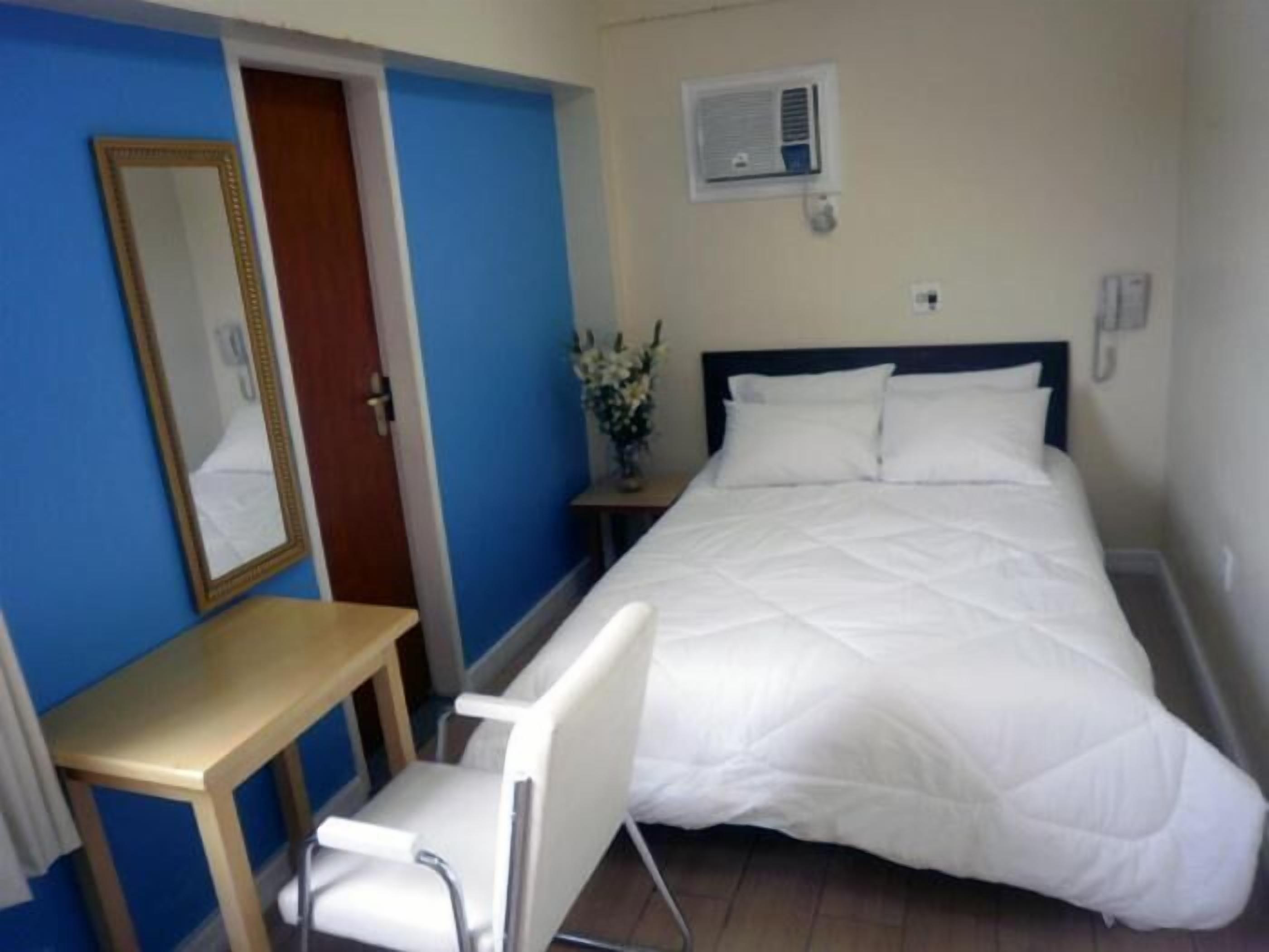 Una habitación de hotel con cama, mesita de noche, silla, espejo y aire acondicionado de pared.