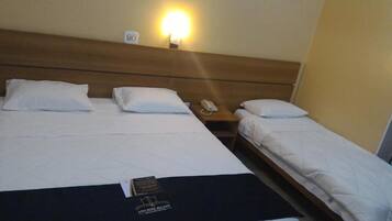 Quarto de hotel com duas camas, uma mesa de cabeceira com abajur e um telefone.