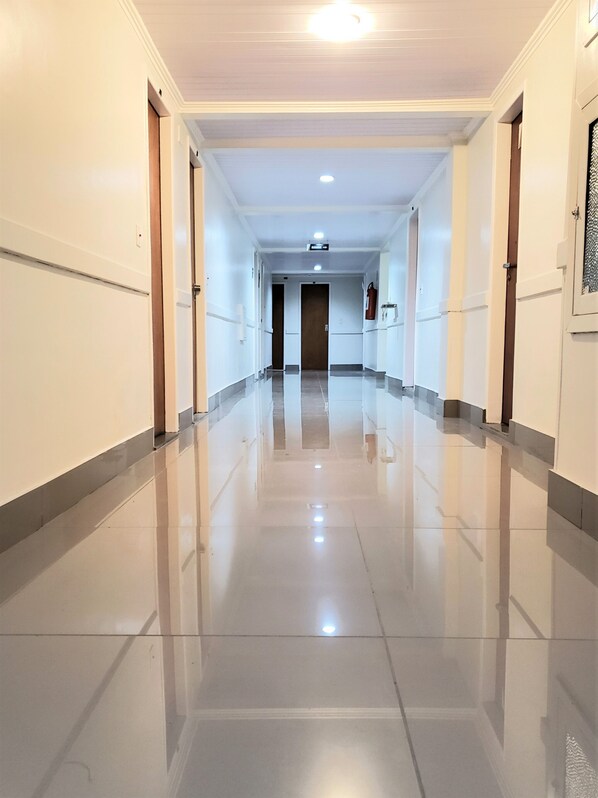 A long, well-lit corridor with a shiny floor, doors on both sides, and a fire extinguisher mounted on the wall.