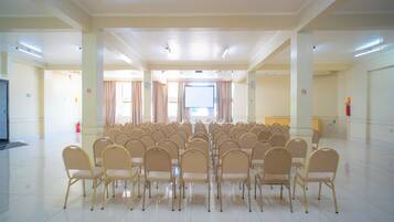 Uma sala de conferências com fileiras de cadeiras, uma tela grande e um palco.