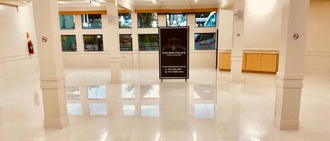 Un vestíbulo amplio con piso pulido, múltiples ventanas y un cartel central para Ang Bom Palace Hotel & Events.