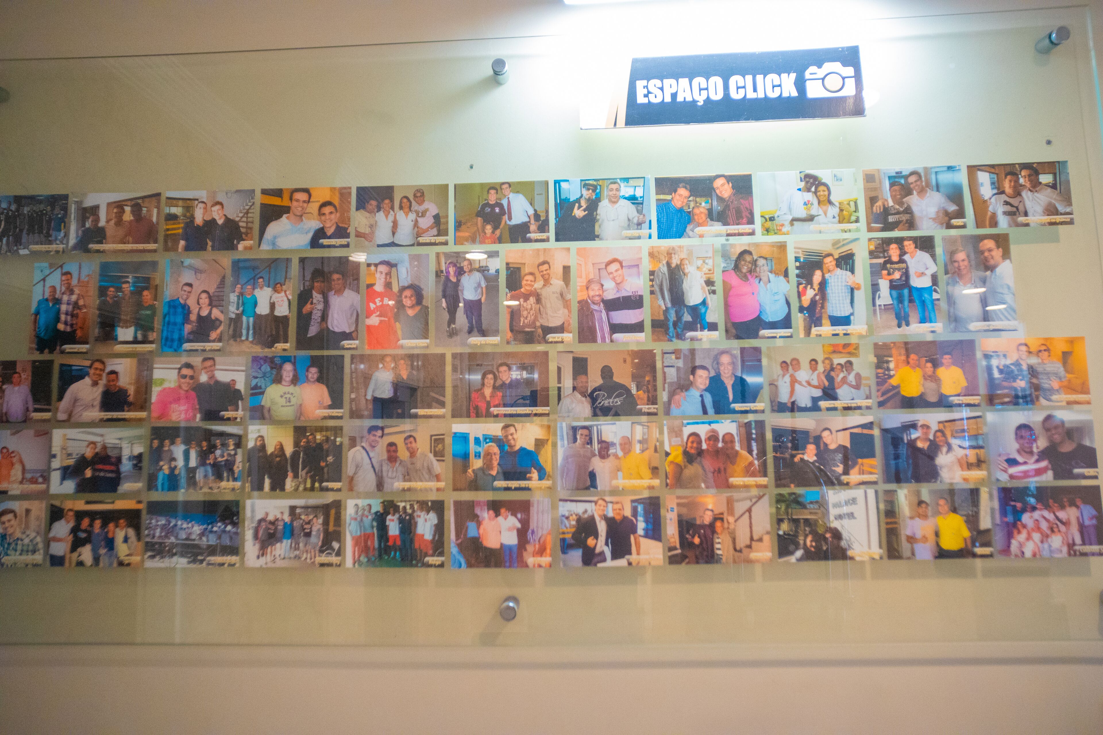 Eine Wand voller Fotos in einem Raum, in dem ein Schild "ESPAÇO CLICK" steht.